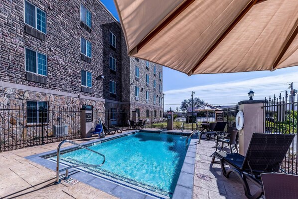 A swimming pool with a stone building in the background, outdoor seating, and a lifeguard stand. - Comfort Suites Grand Prairie - Arlington North (Grand Prairie)