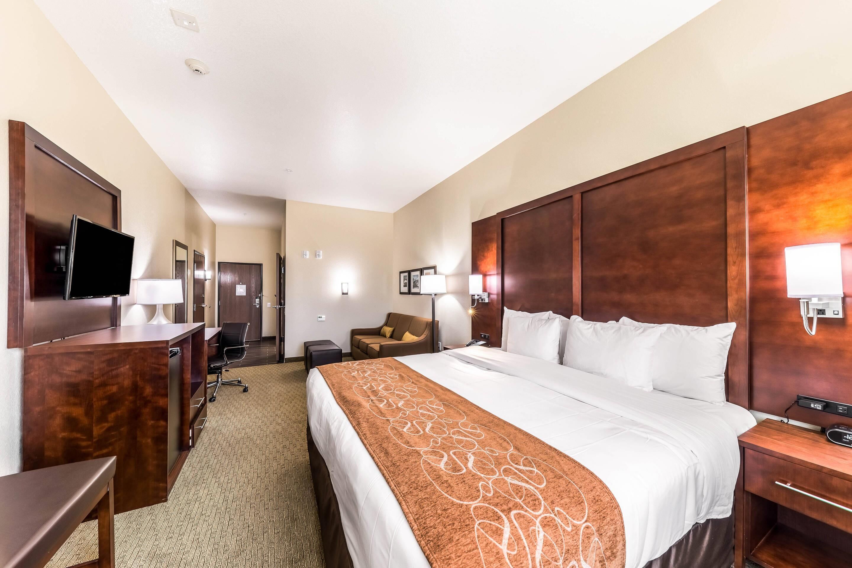A hotel room with a large bed, a desk, a television, and a seating area.