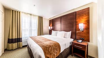Habitación de hotel con una cama grande, una mesita de noche con teléfono, una lámpara de pared y un ventanal con cortinas.