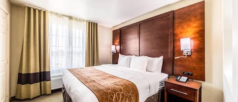 A hotel room with a large bed, a bedside table with a phone, a nightstand, a wall-mounted lamp, and a window with curtains.