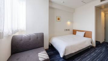 A hotel room with a bed, a sofa, a wall-mounted light, and a small picture.