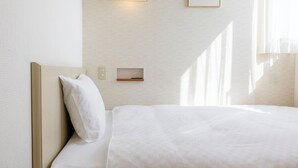 Een net opgemaakt bed met een kussen, nachtkastje en een wandlamp.