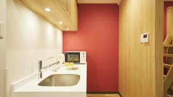 A compact kitchen with a white countertop, stainless steel sink, and a microwave.