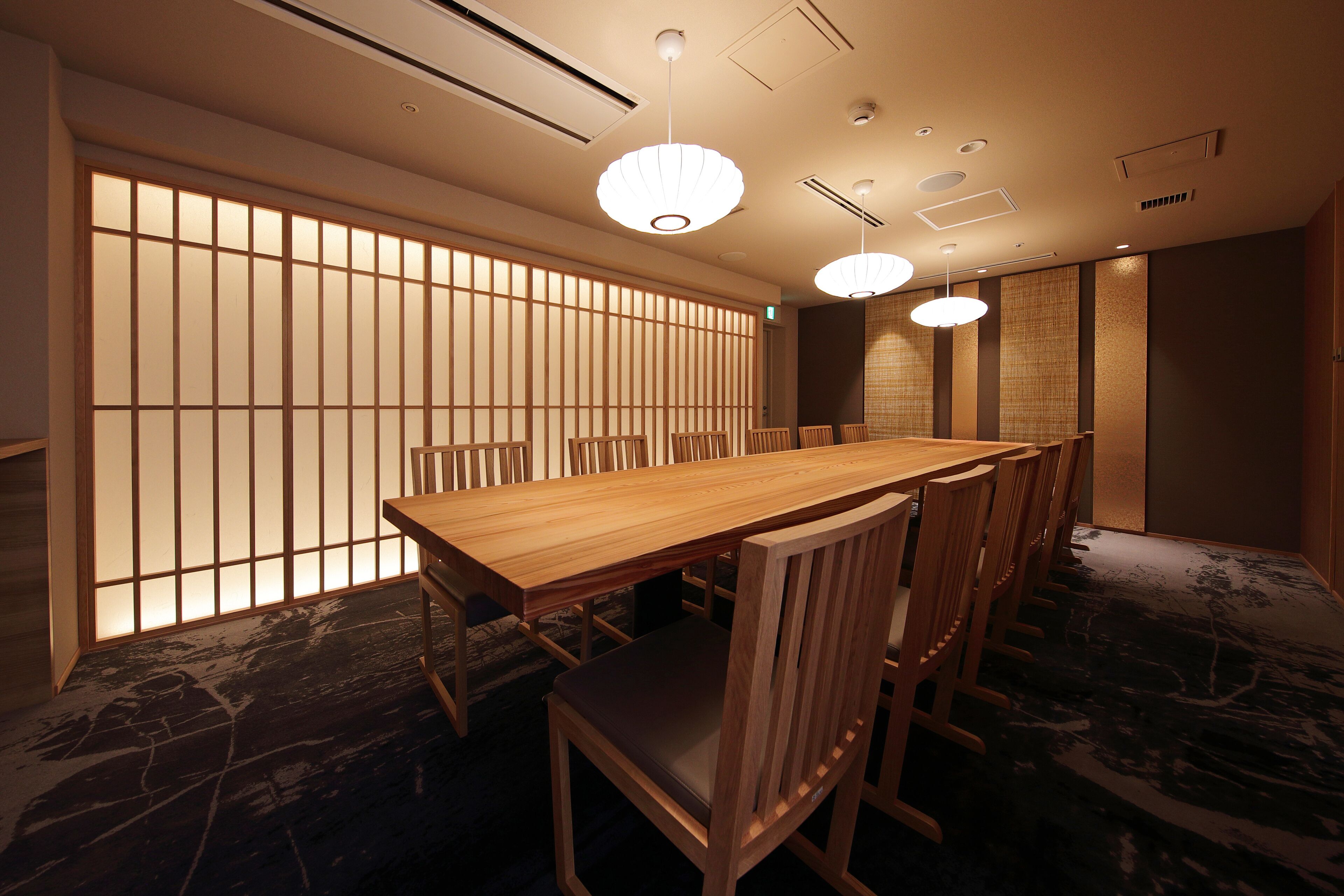 A traditional Japanese-style room with a long wooden table and chairs, a shoji screen, and hanging pendant lights.