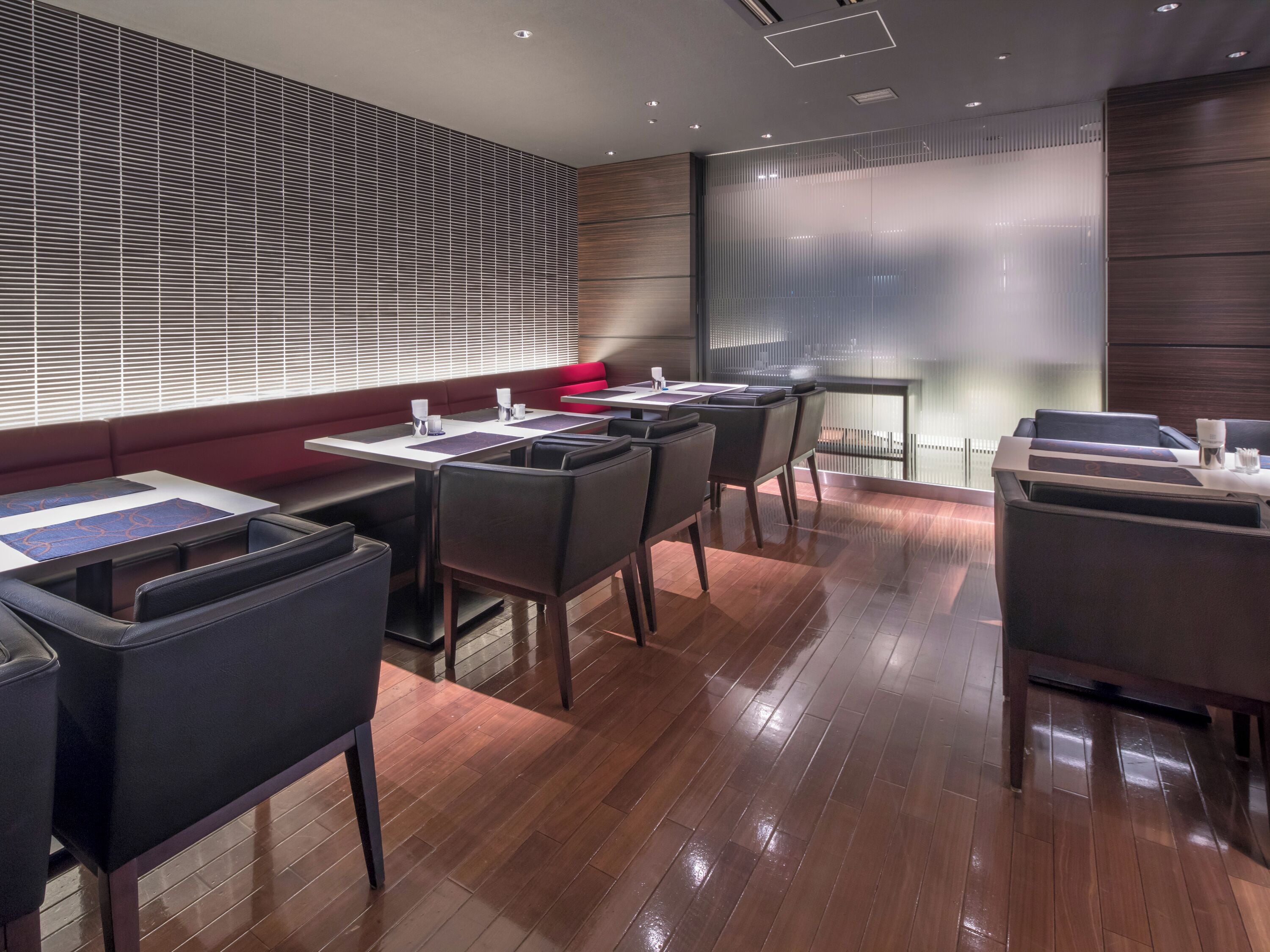 A modern conference room with a large glass wall, wooden flooring, and a red cushioned bench.