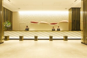 A reception area with a modern design, featuring a reception desk, two chairs, and a decorative wall with a textured pattern. - ART HOTEL Osaka Bay Tower (Osaka)