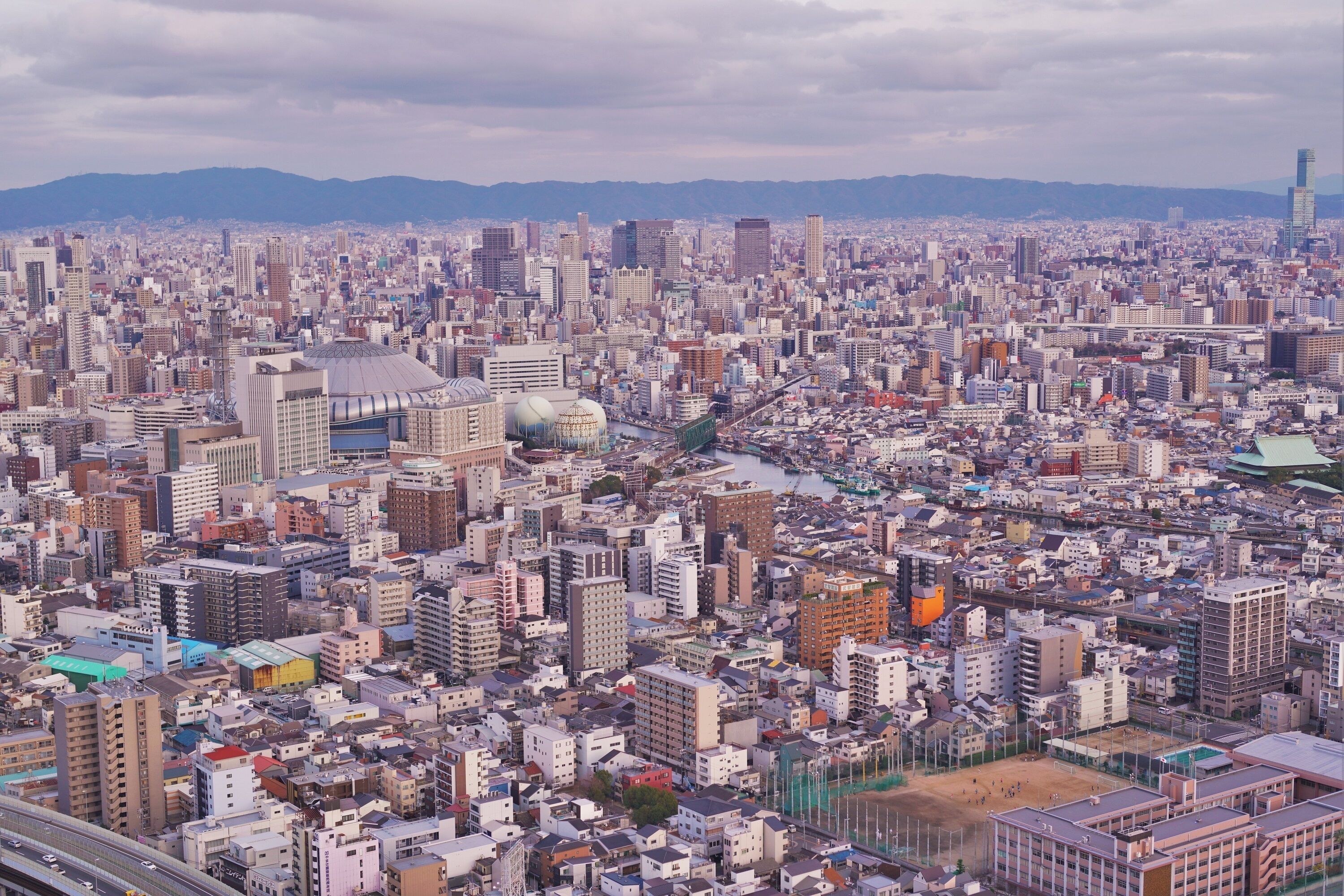 A densely packed urban cityscape with numerous buildings, a prominent dome structure, and a river running through the center.