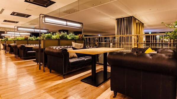 A modern restaurant with black leather booths, a wooden table, and plants in the center. - ART HOTEL Osaka Bay Tower (Osaka)