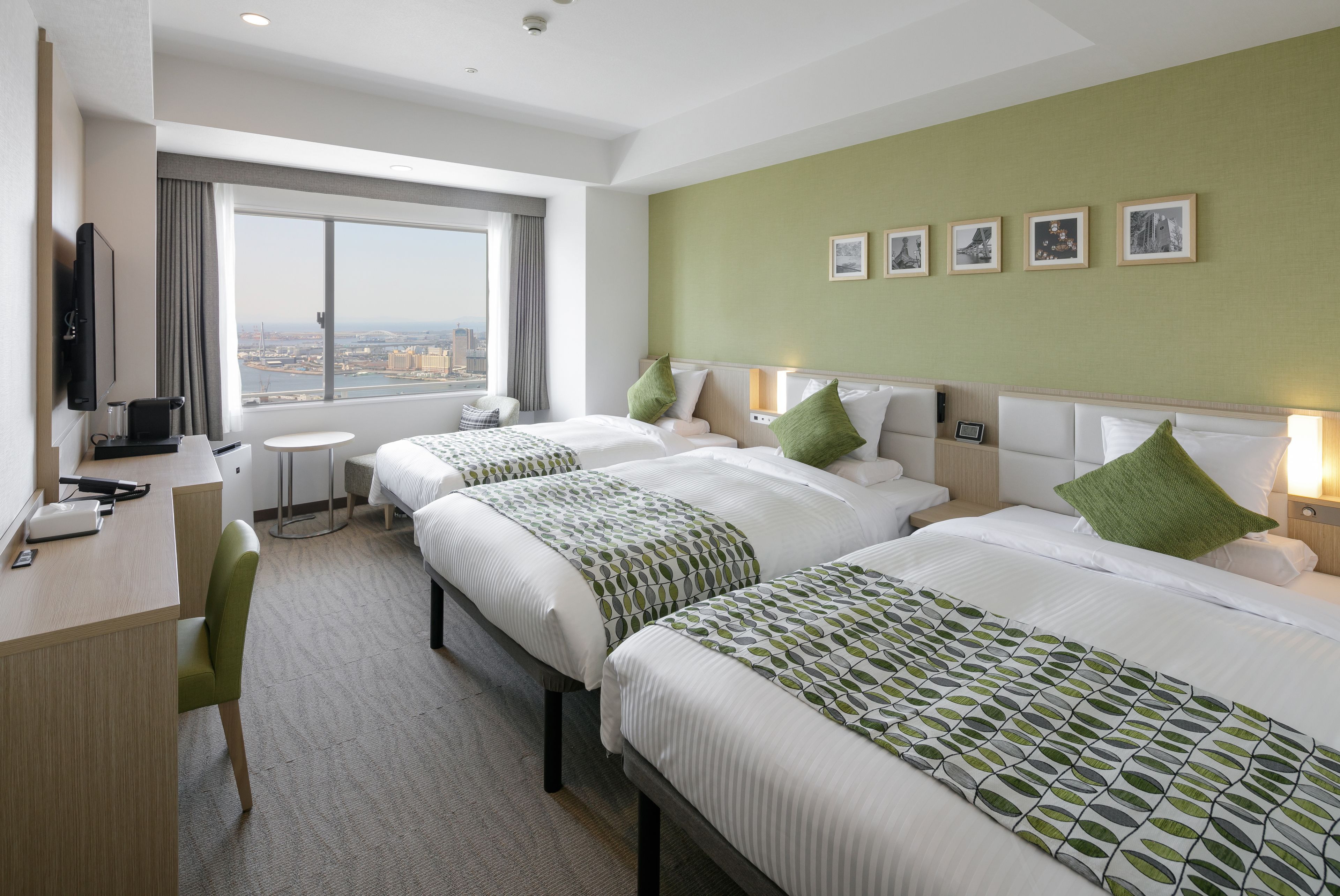 Habitación de hotel con dos camas, un escritorio, una silla, un televisor y un ventanal con vistas a la ciudad.