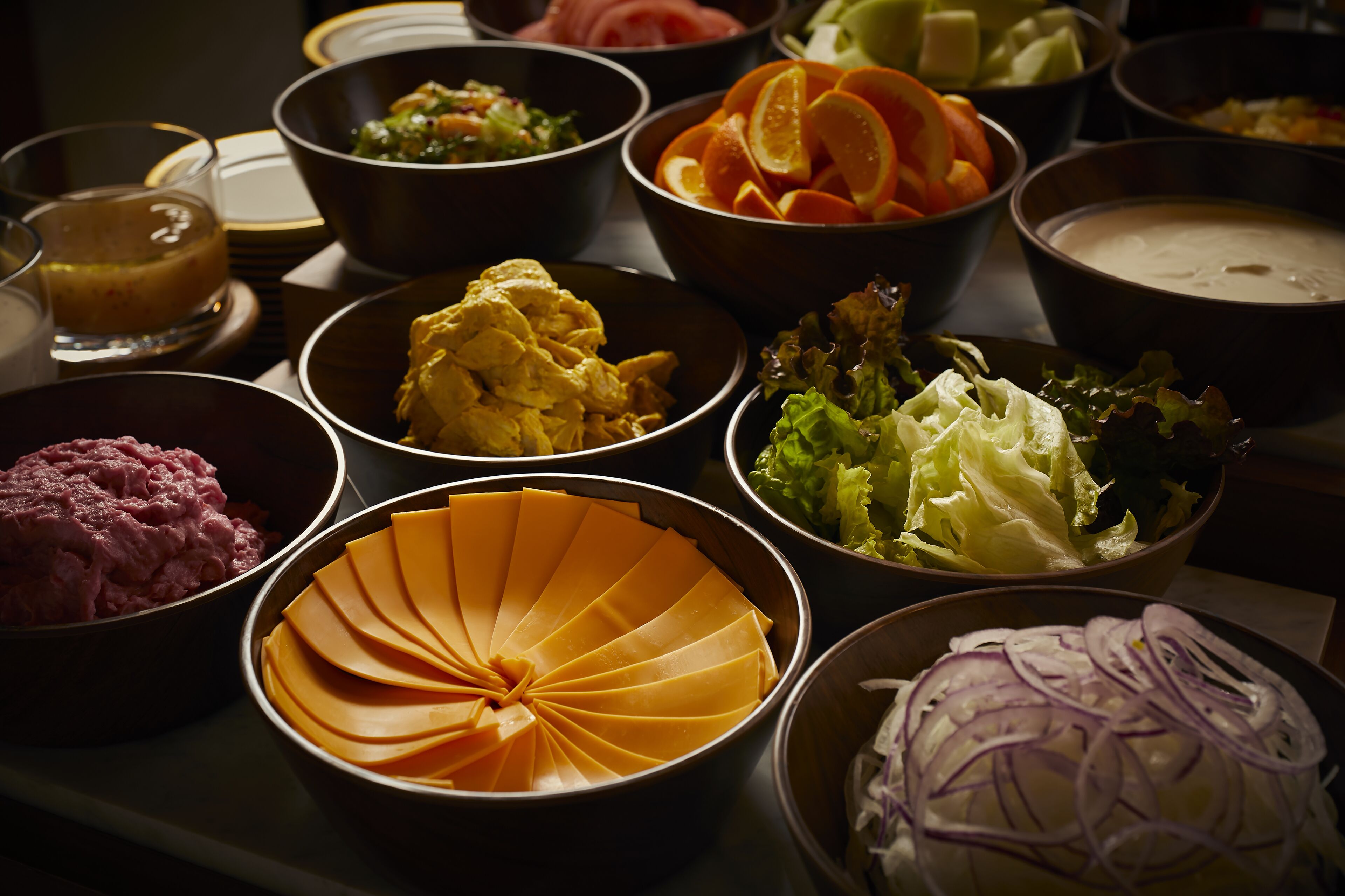 A variety of food items arranged on a table, including sliced vegetables, a bowl of meat, and a dish with a yellow sauce.