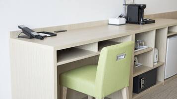 A modern hotel room with a wooden desk, a green chair, a coffee maker, and a mini-fridge.