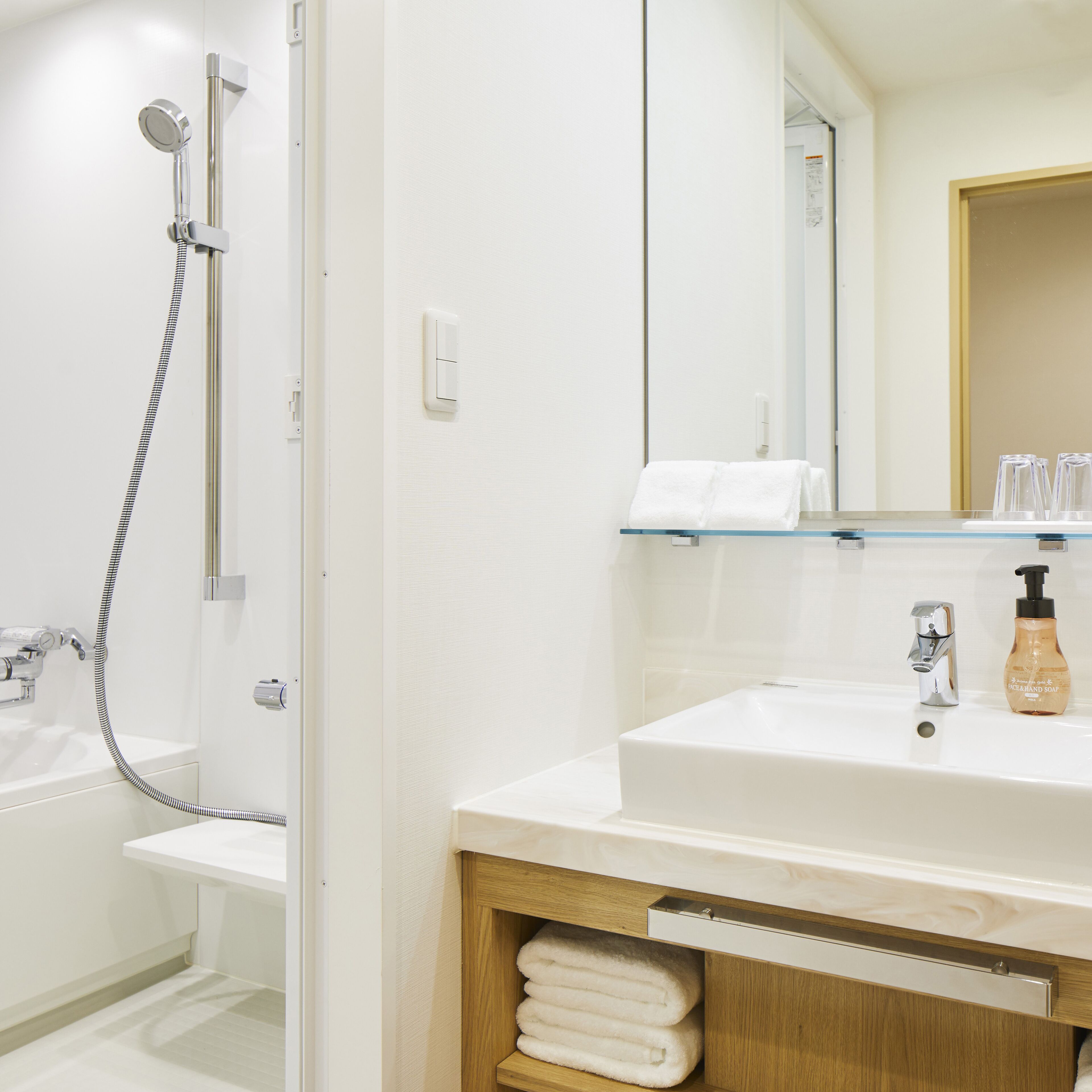 A modern bathroom with a white sink, a glass shelf, a wooden cabinet, and a shower area.