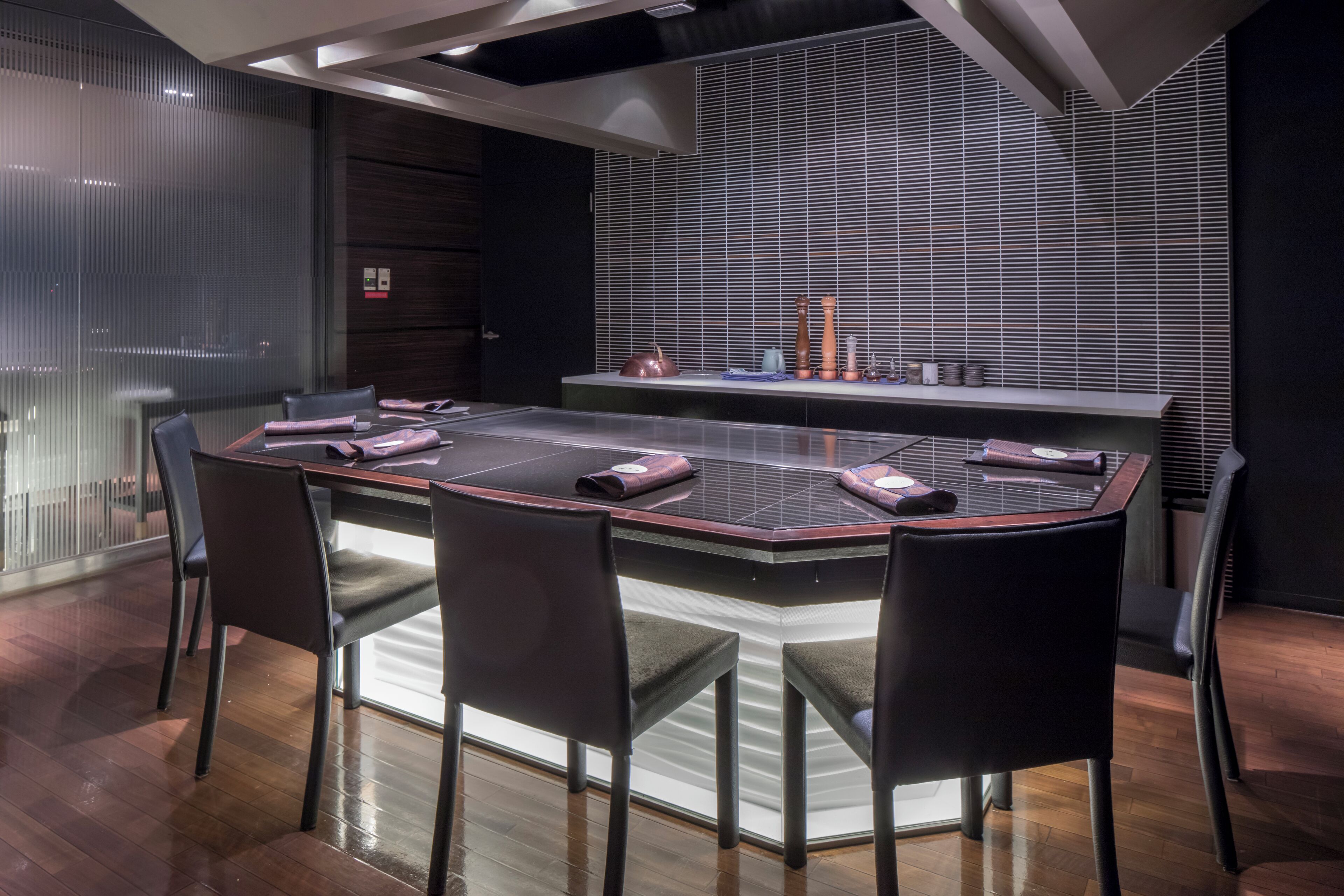 A modern conference room with a glass table, black chairs, and a dark wooden accent wall.