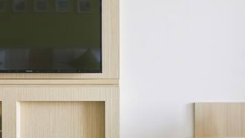 Et moderne interiør med et fladskærms-tv monteret på et træskab, en glasmontre med en sort genstand, og et pengeskab med et tastatur.