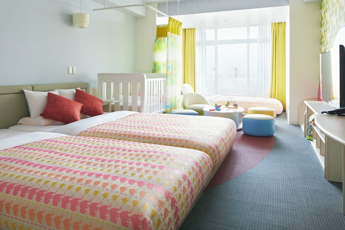 A hotel room with two beds, a desk, a chair, and a small table with toys.