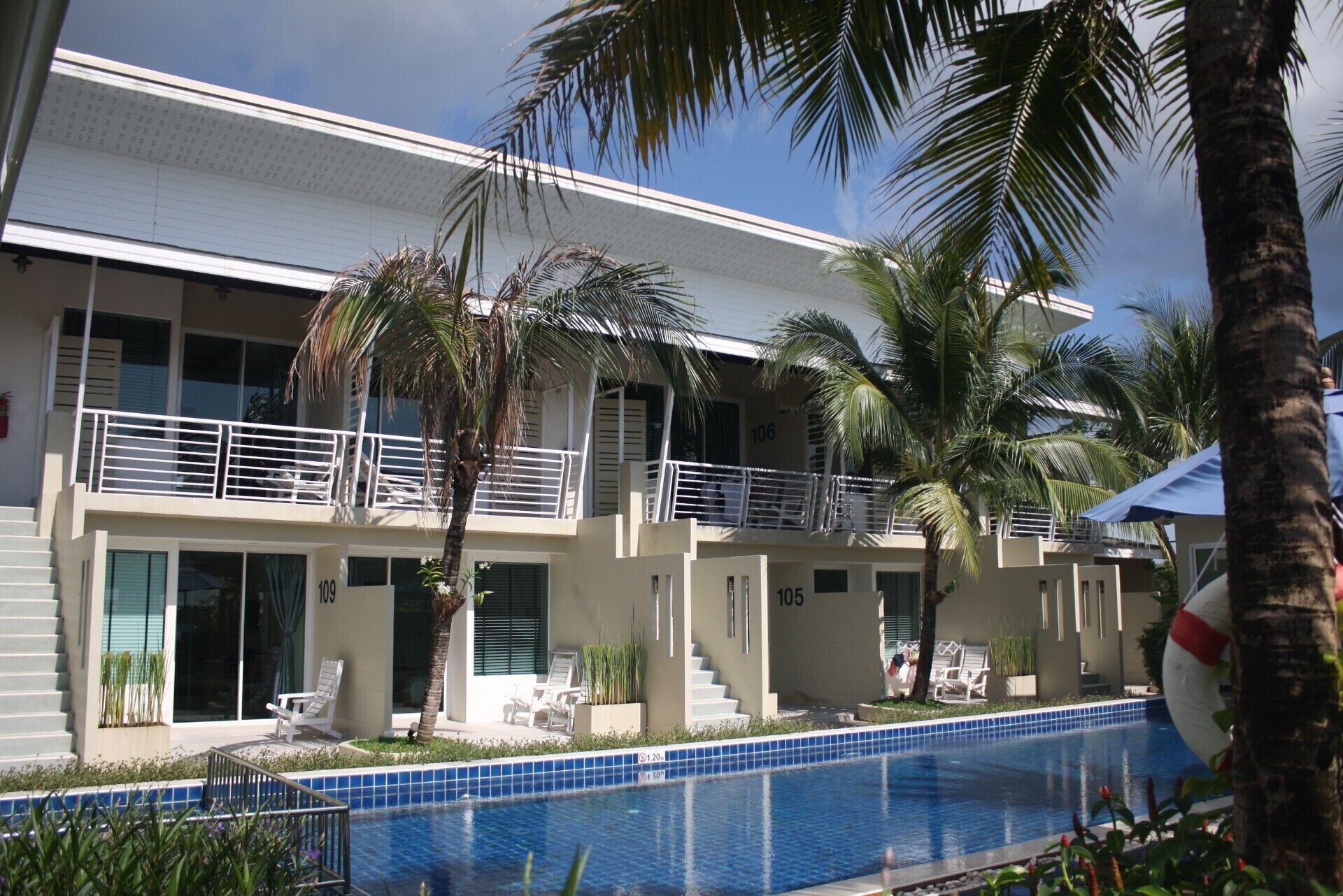 Un hotel con piscina, palmeras y un edificio de dos pisos con balcones.