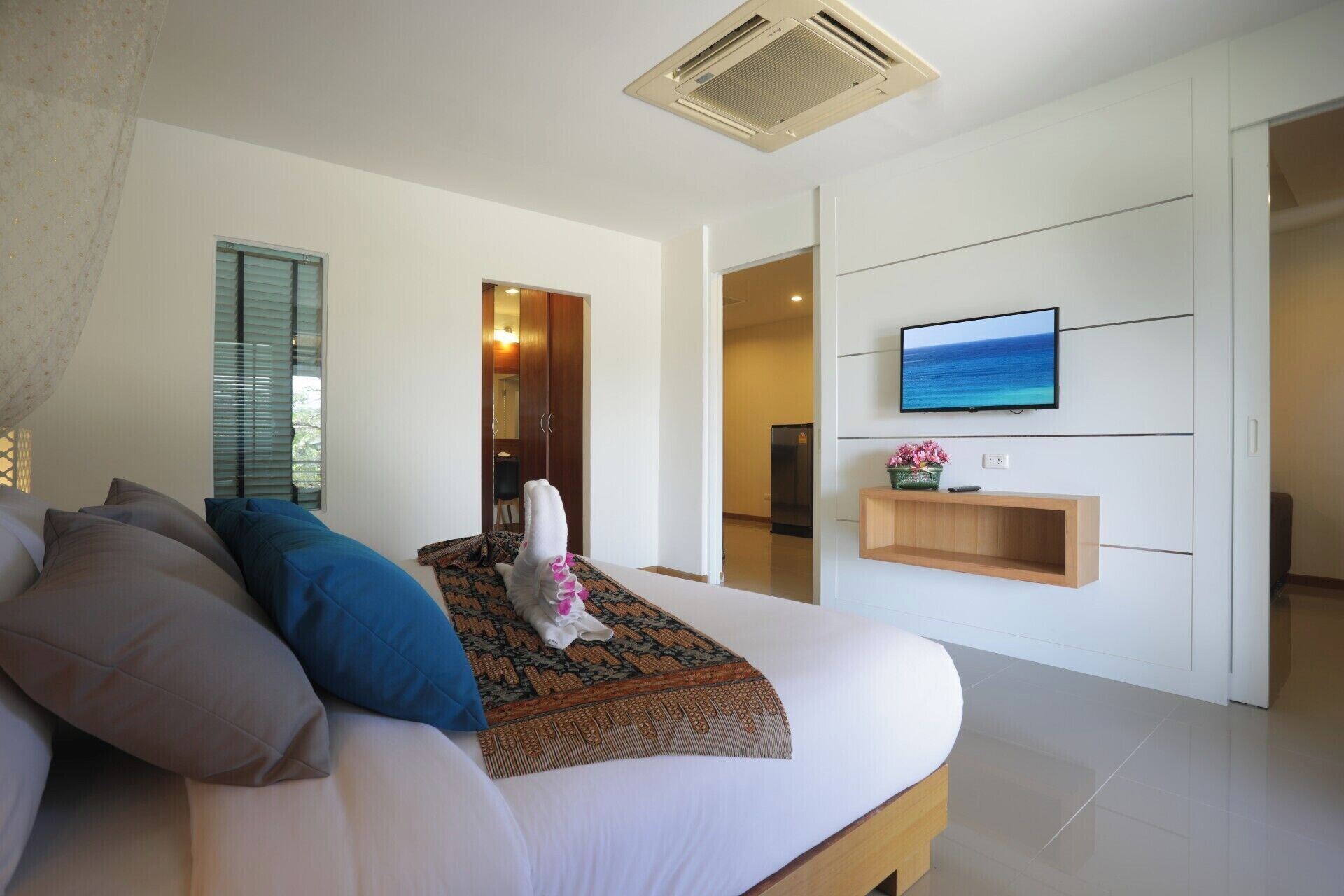 A modern hotel room with a bed, a TV mounted on the wall, and a small wooden shelf.