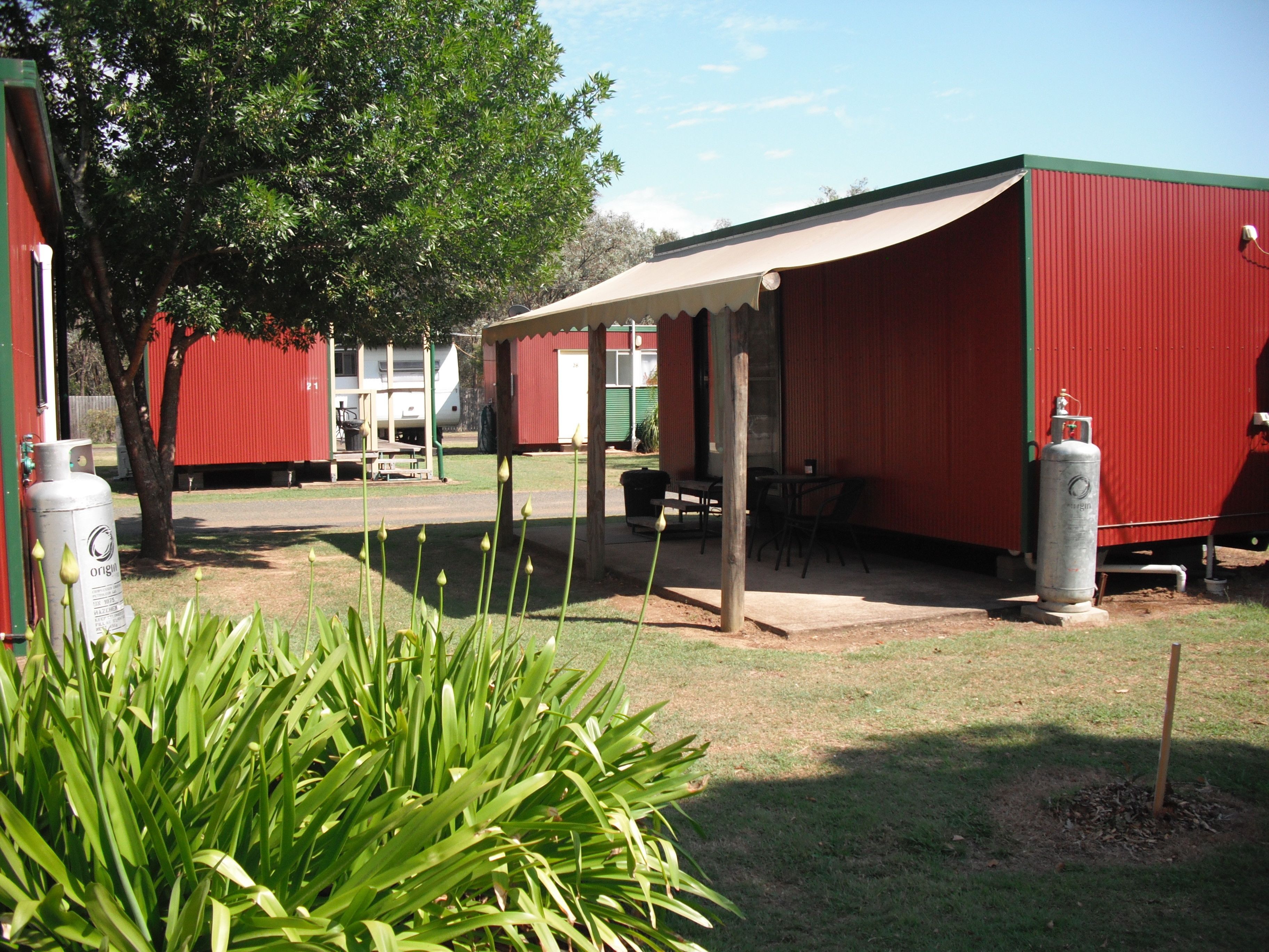 A red building with a covered patio area, a gas cylinder, and a tree in the foreground.