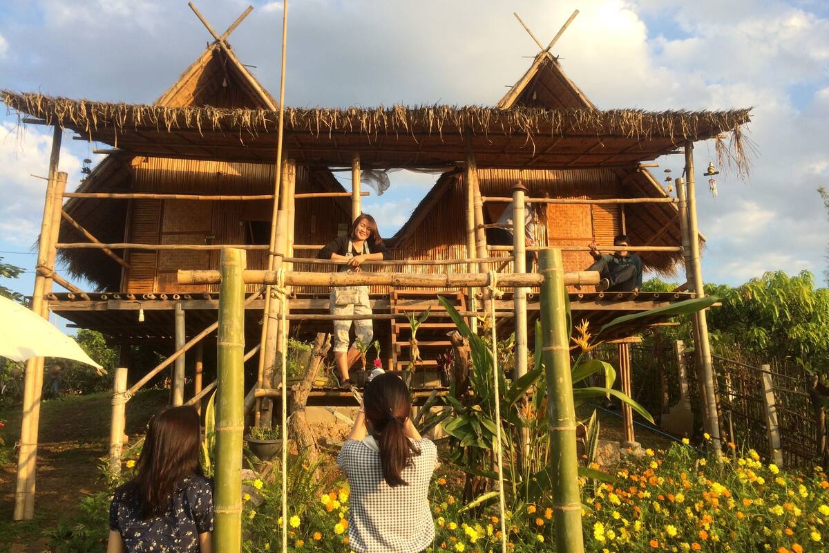 Una estructura tradicional de bambú con techo de paja, rodeada por un jardín con diversas flores.
