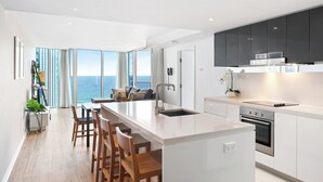 A modern kitchen with a large island, white cabinetry, and a view of the ocean.