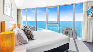 A hotel room with a large bed, a view of the ocean, and a cityscape in the background.