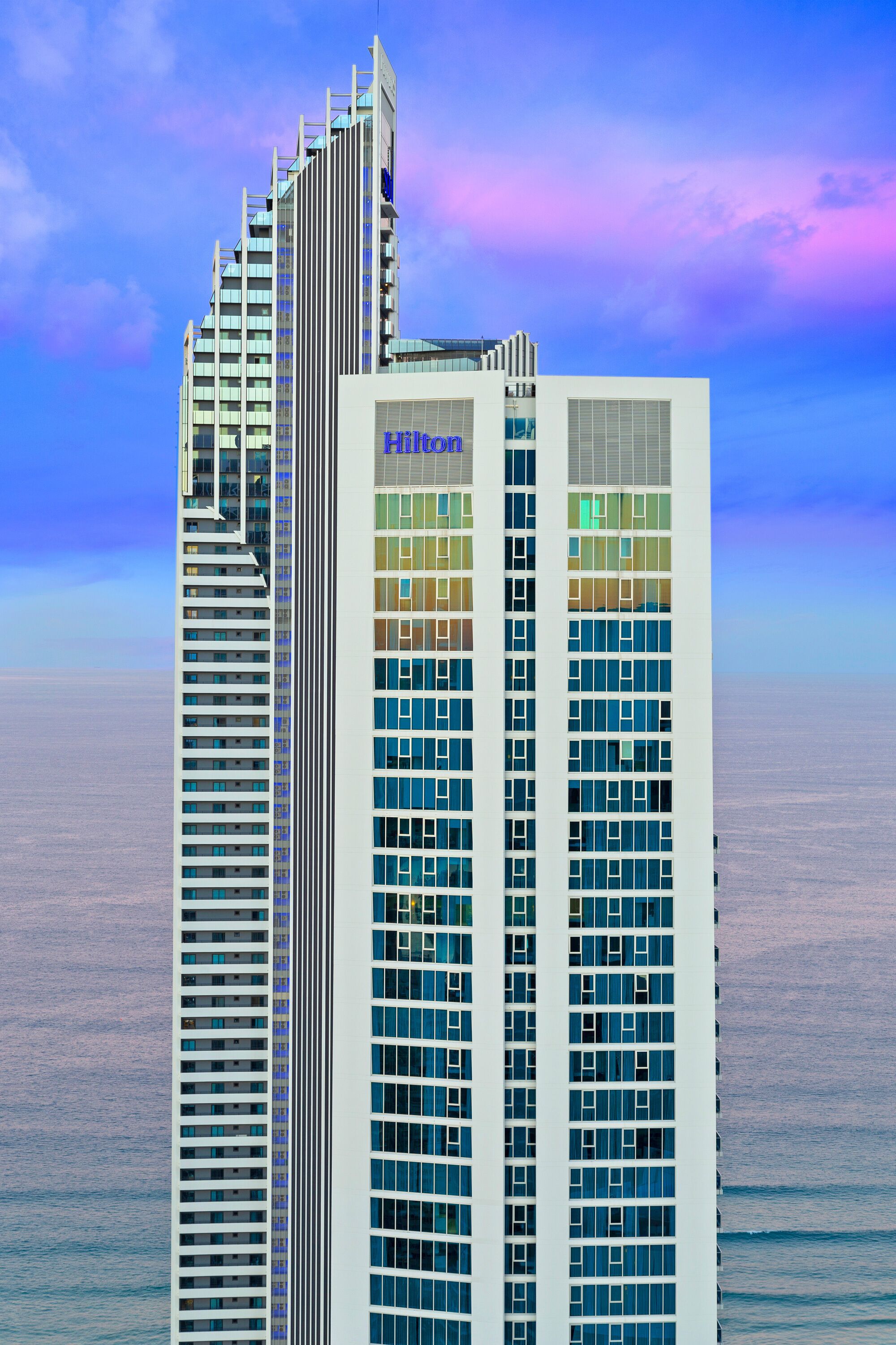 Ett högt hotell med en modern design, som har flera våningar och en tydlig skylt med texten ”Hilton”.