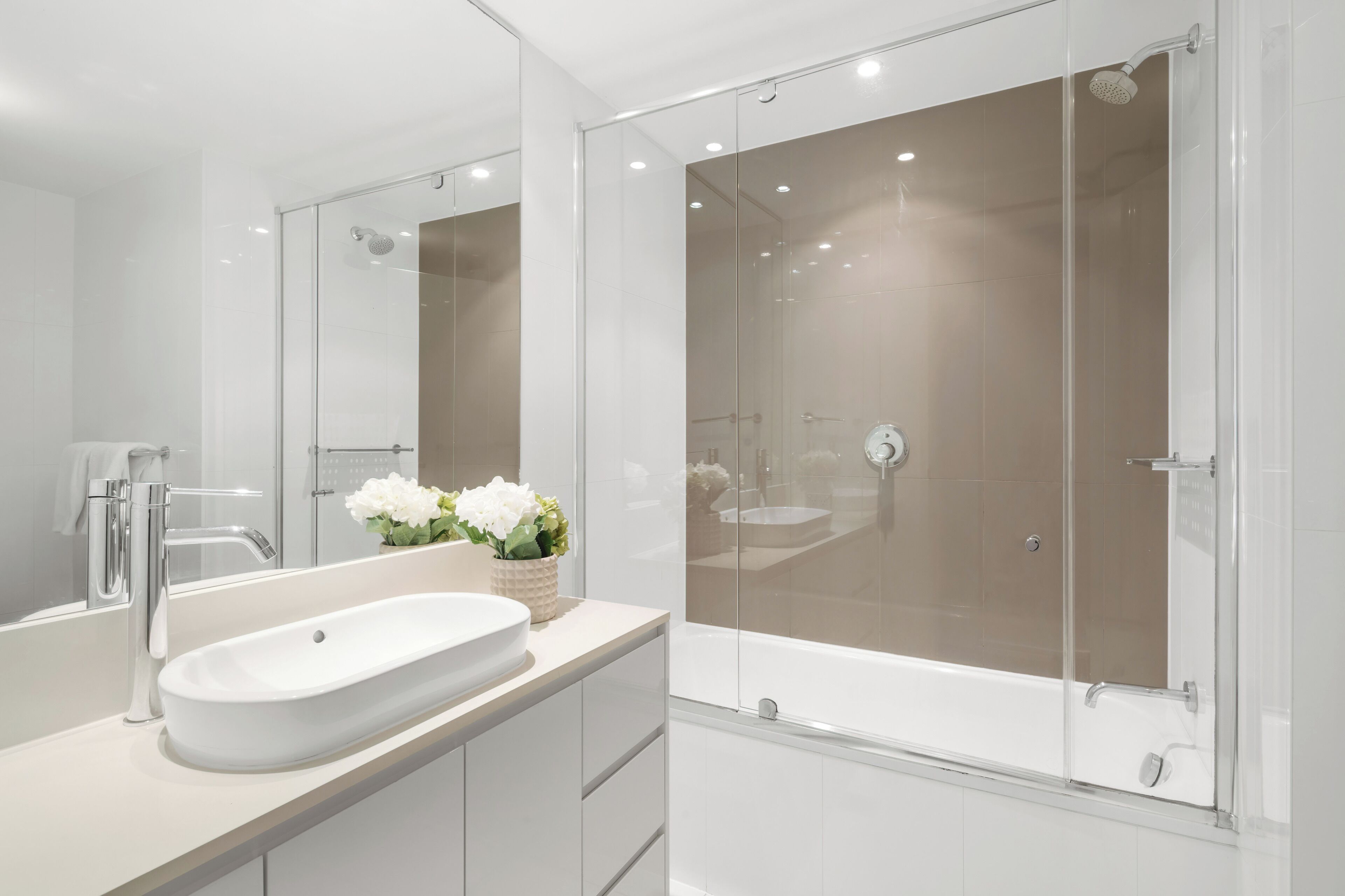 A modern bathroom with a large mirror, a white sink, and a glass-enclosed shower area.