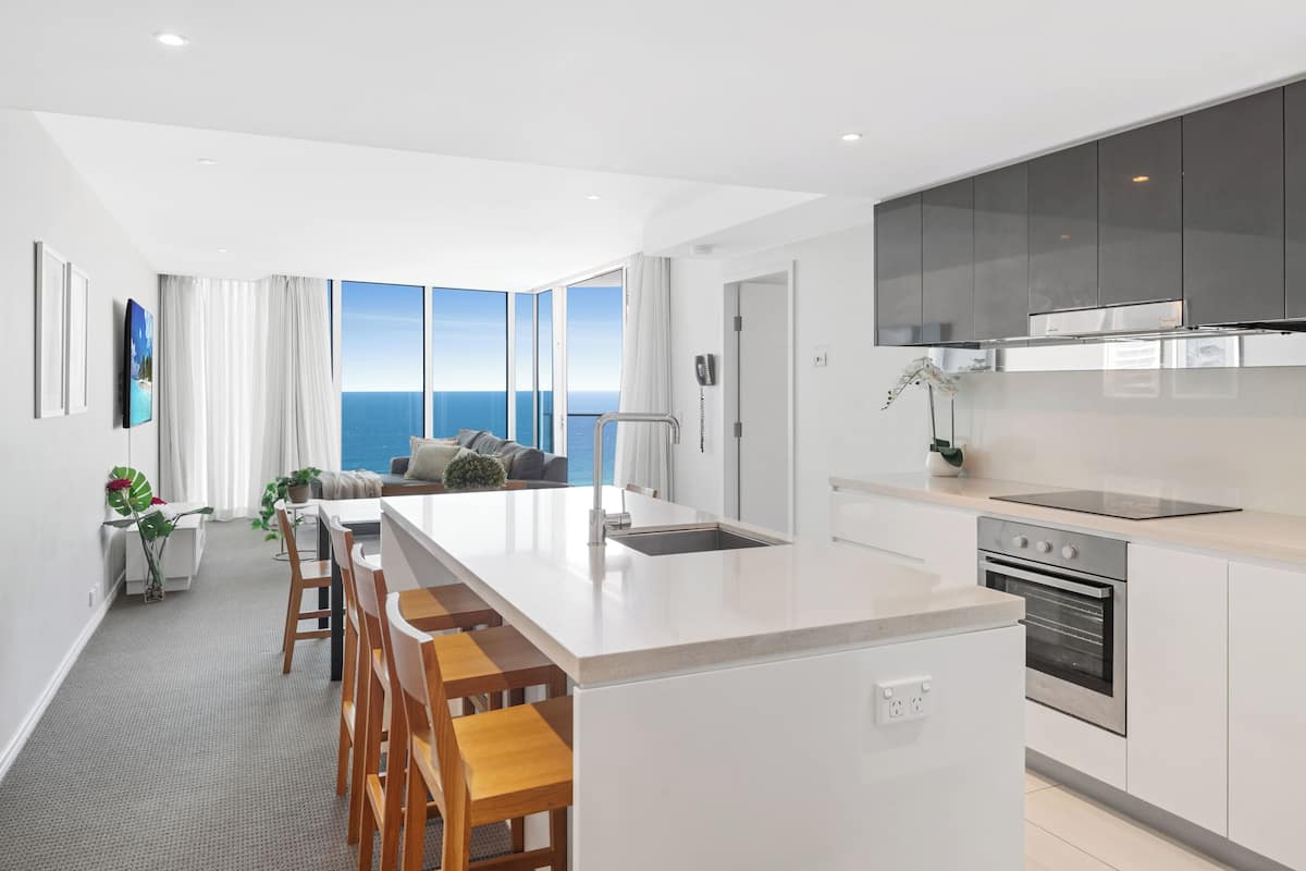 A modern kitchen with a large island, a built-in oven, and a view of the ocean.