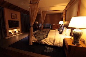 Een slaapkamer met een hemelbed, een aan de muur bevestigde televisie en een nachtkastje met een lamp.
