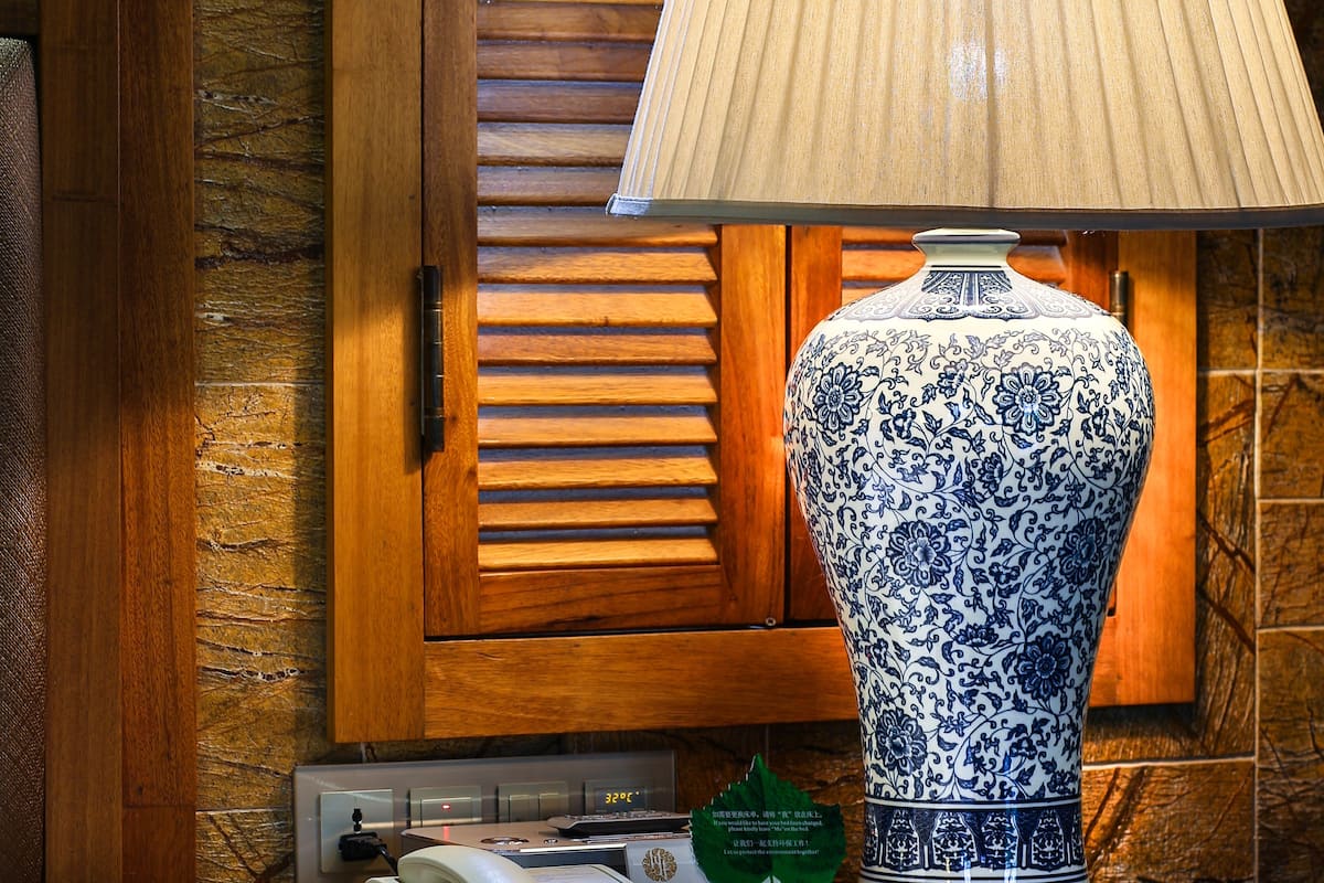A traditional blue and white ceramic lamp on a bedside table, a telephone, and a small green sign with text.