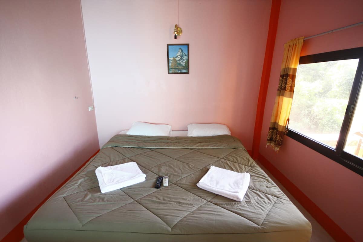 Cama individual con colchón acolchado, dos almohadas y dos toallas dobladas. Un control remoto está sobre la cama.