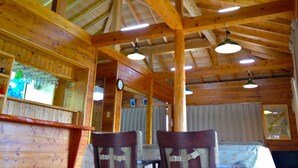 A wooden interior with a high ceiling, exposed beams, and hanging lights. There are two chairs and a table with a white tablecloth. - Churahashi (Nakijin)