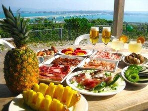 A table with various food items and drinks, a pineapple, and a view of a bridge over water.
