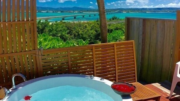 A hot tub on a wooden deck with a view of a beach and palm tree. - Churahashi (Nakijin)