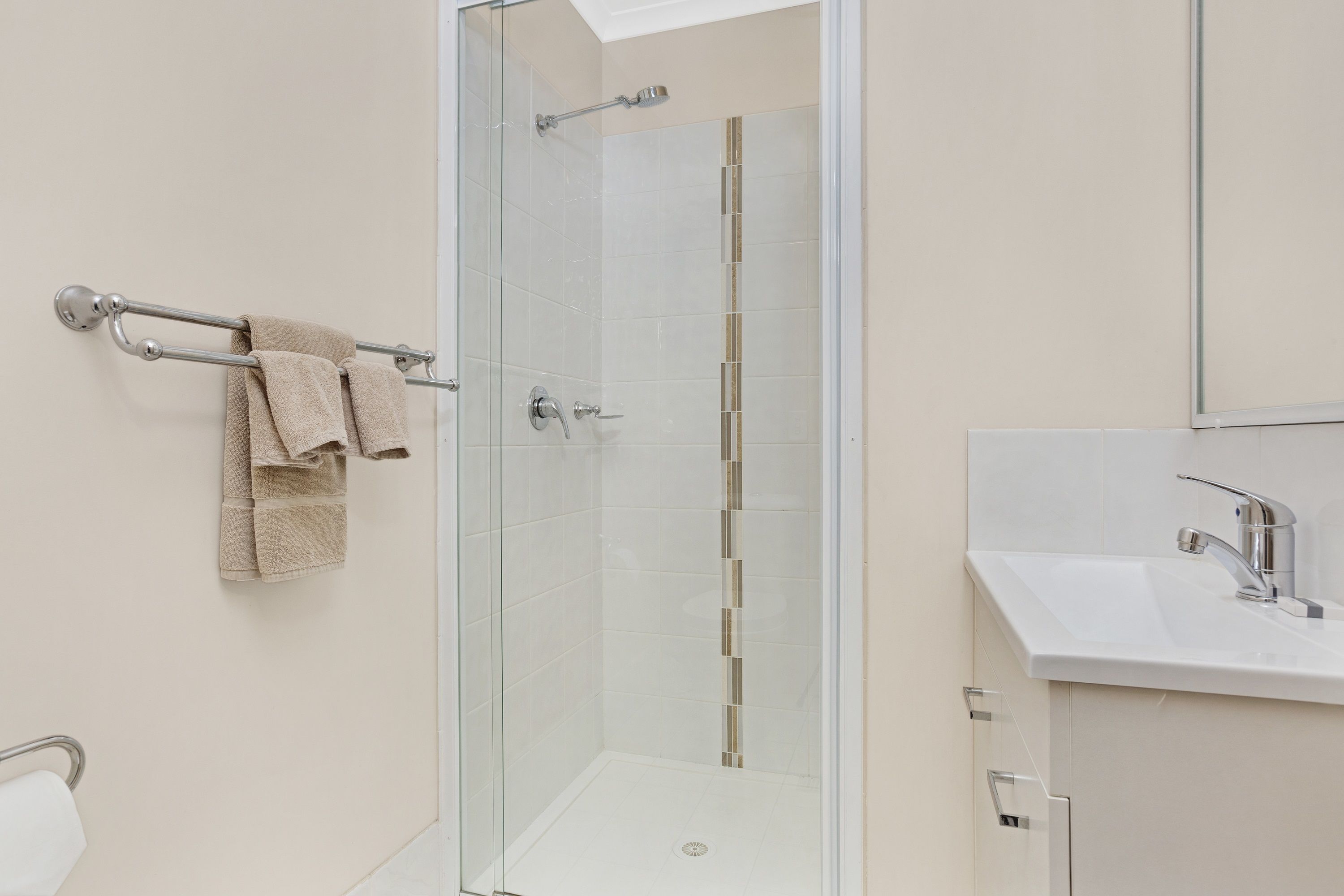 A modern bathroom with a glass-enclosed shower, a white sink, and a towel rack with a beige towel.
