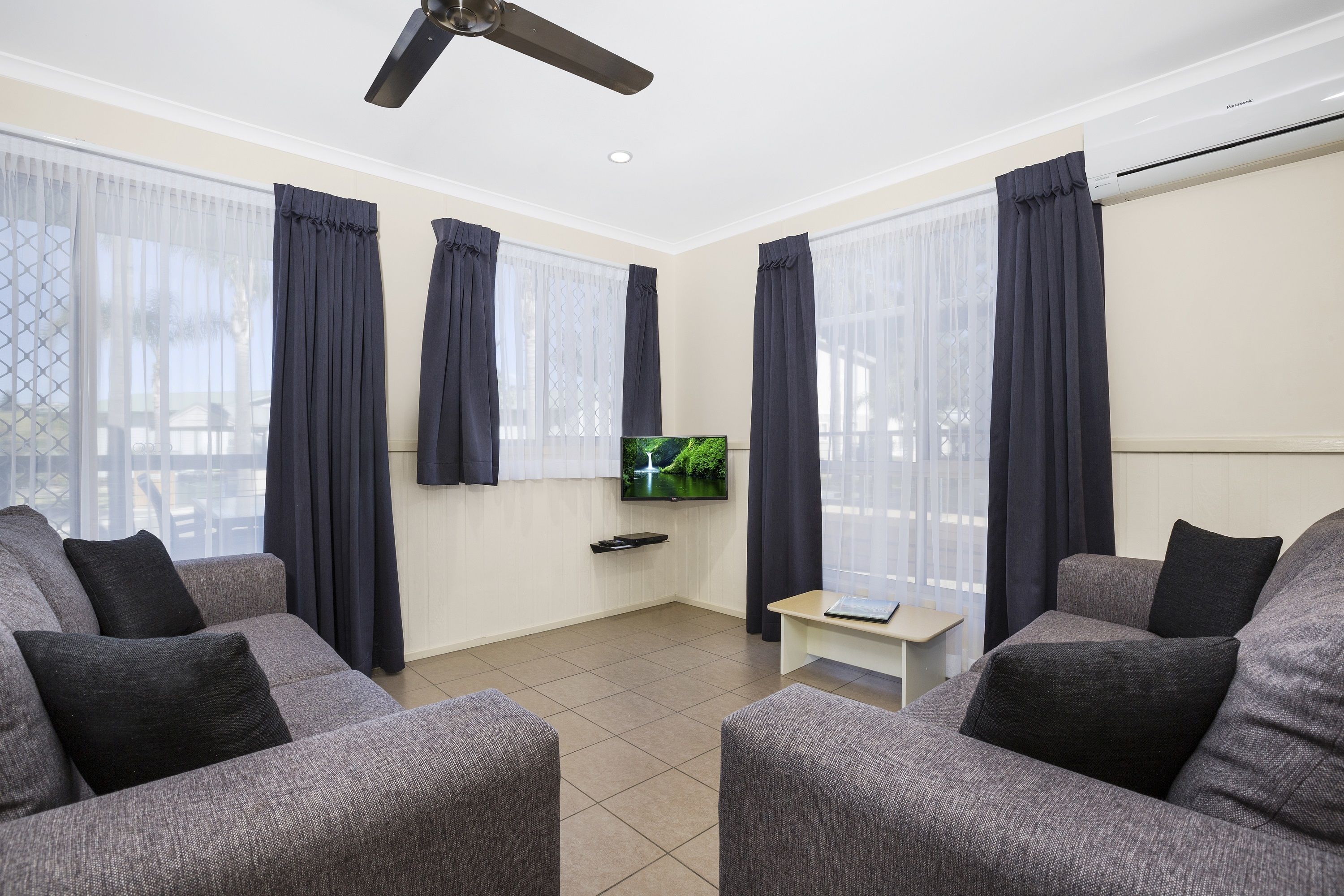 A modern living room with grey sofas, a flat-screen TV, and a ceiling fan.