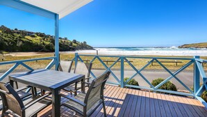 Um deck de madeira com mesa e cadeiras, com vista para uma praia e ondas.