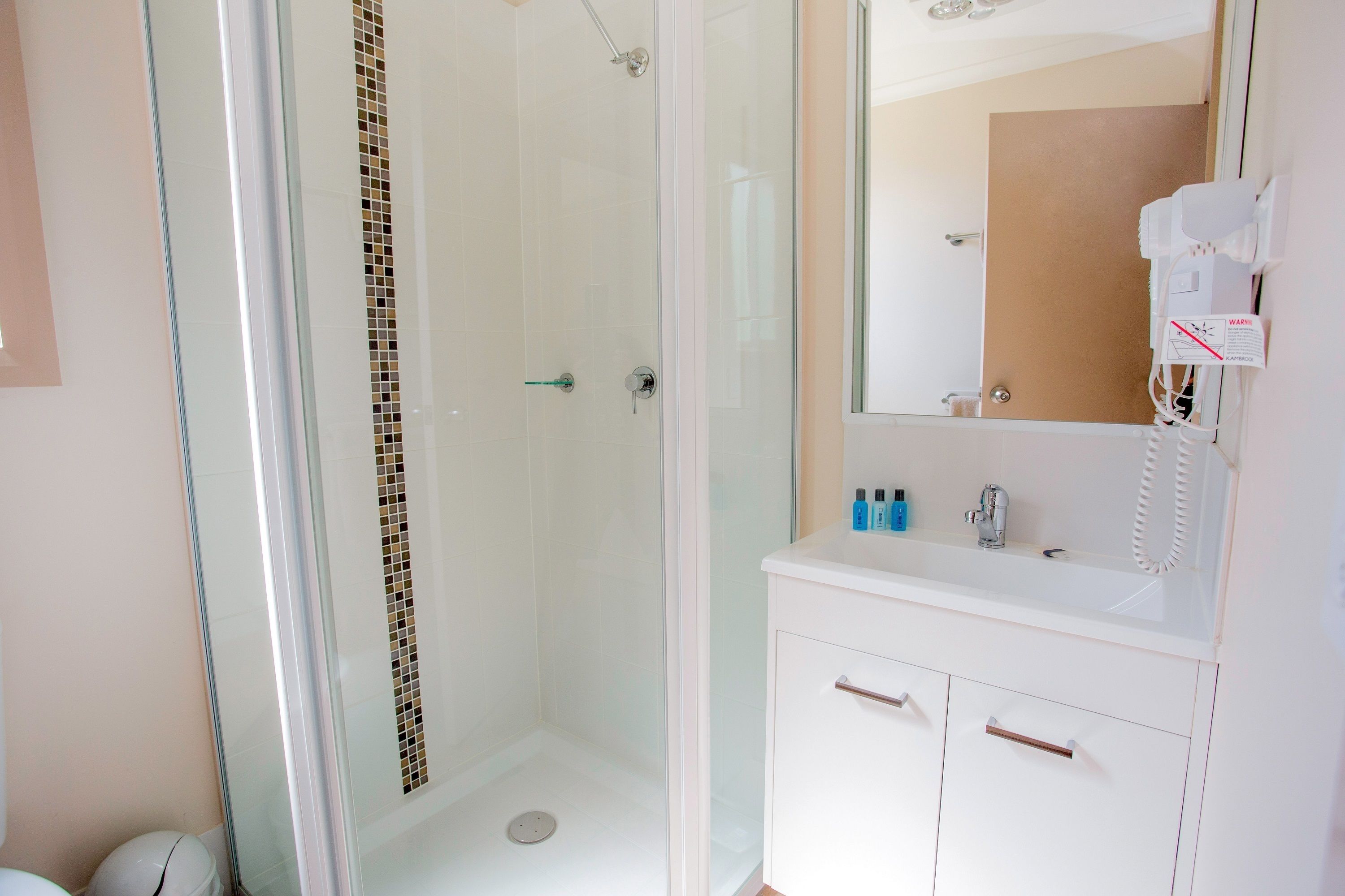 A modern bathroom with a glass-enclosed shower, white vanity with a mirror, and a hairdryer on the wall.