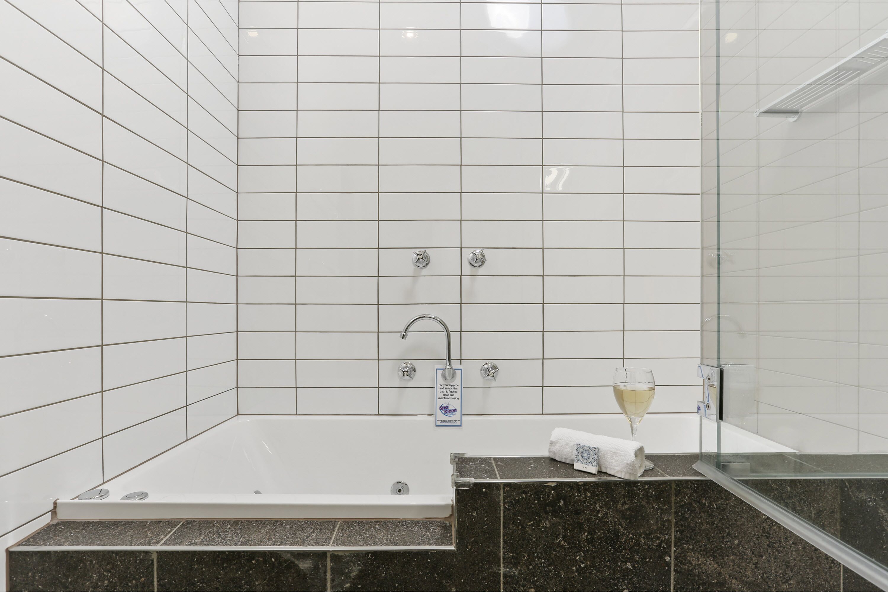 A modern bathroom with white tiled walls, a glass shower enclosure, a bathtub, and a marble countertop.