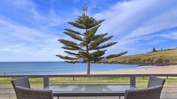 Une terrasse avec des chaises et une table en osier, donnant sur une plage et l’océan.