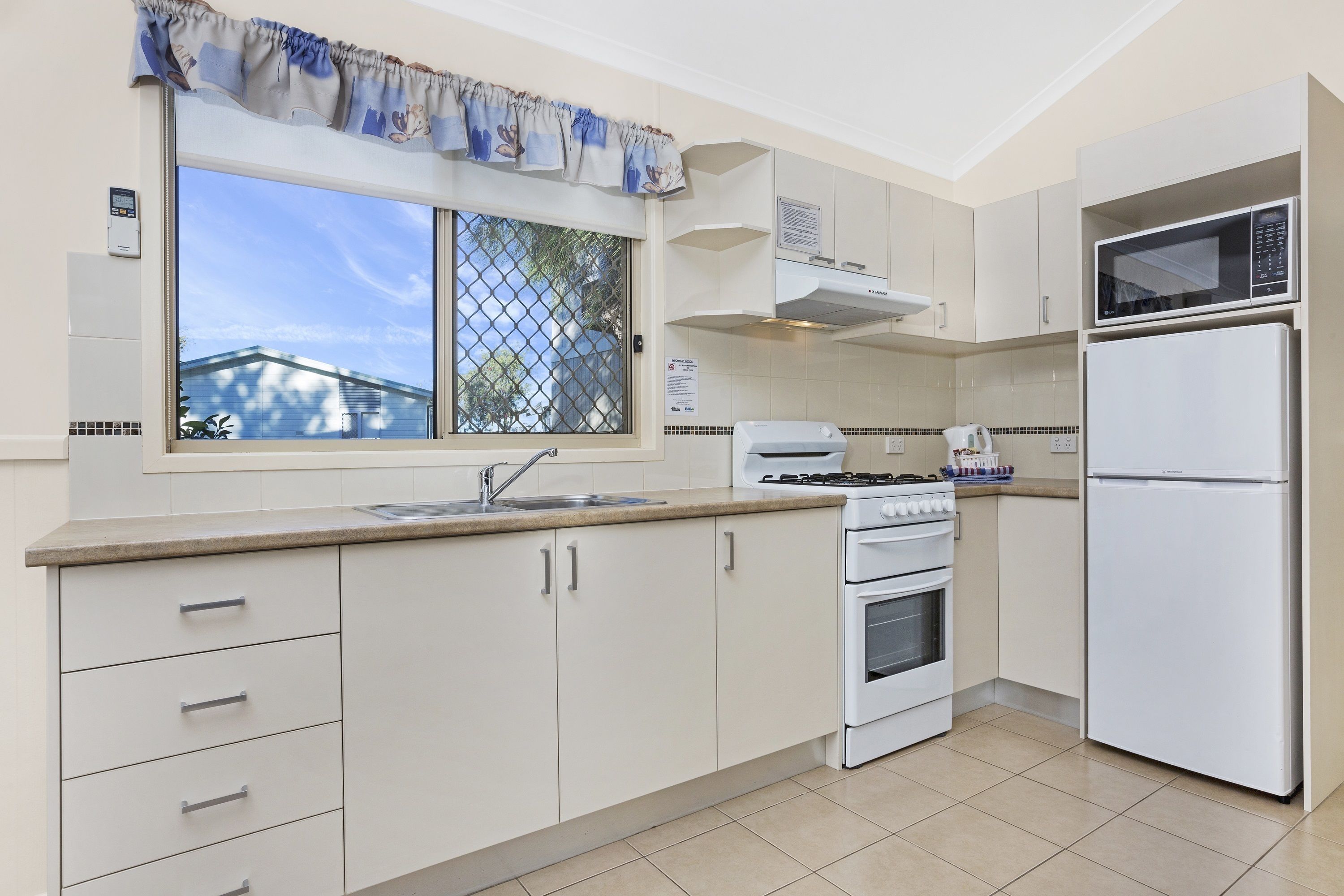 A kitchen with white cabinets, a stove, a sink, a microwave, and a refrigerator.