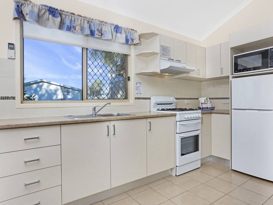 Una cocina con armarios blancos, estufa, fregadero, microondas y refrigerador.