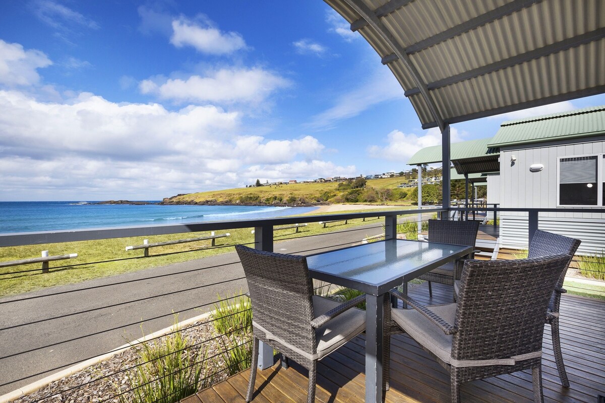 A covered outdoor seating area with a table and chairs, overlooking a beach and ocean.
