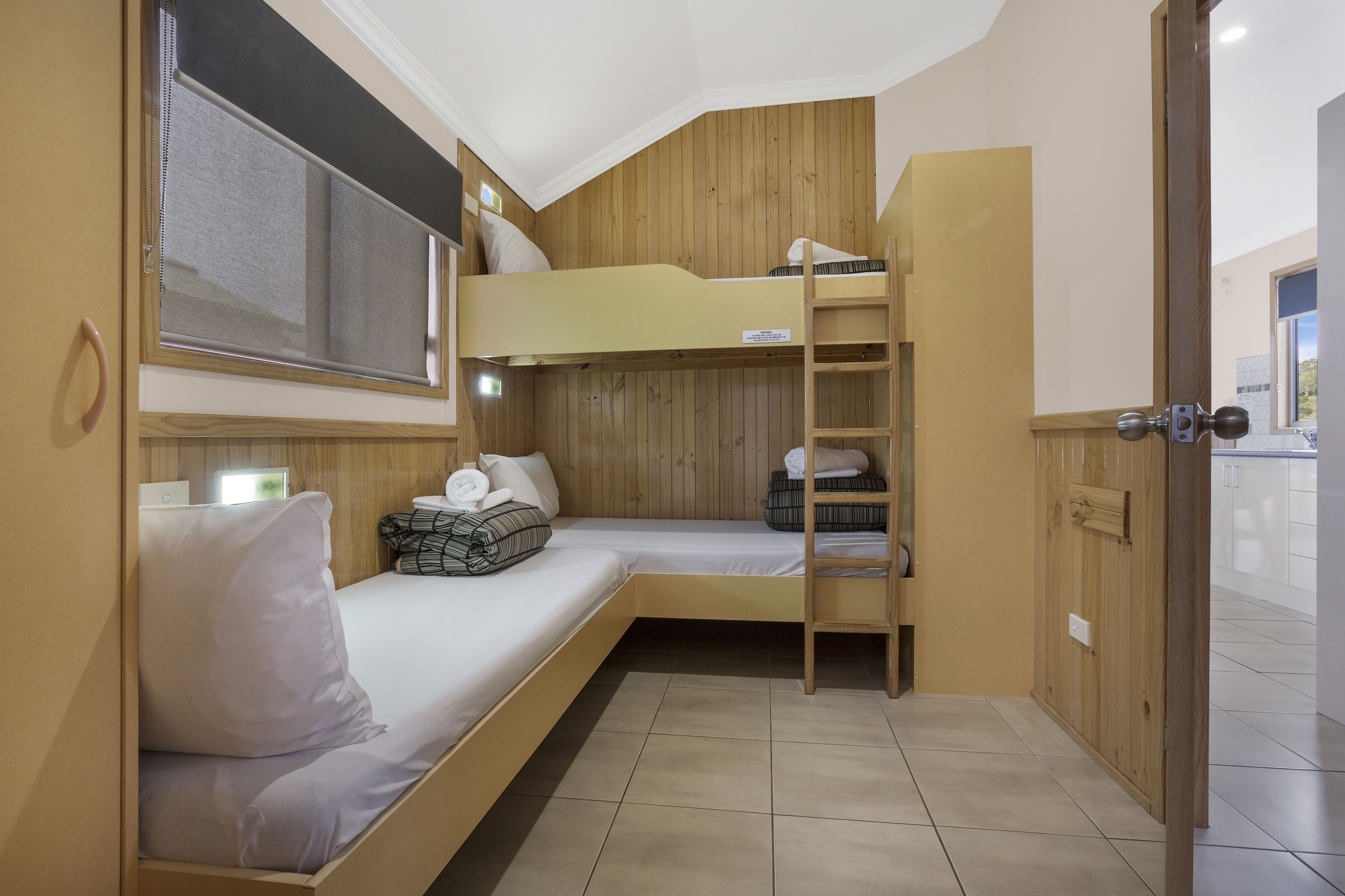 A compact room with a bunk bed, a small desk, and a window with blinds.