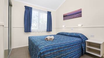 Un dormitorio con una cama, cortinas, un cuadro y una estantería.