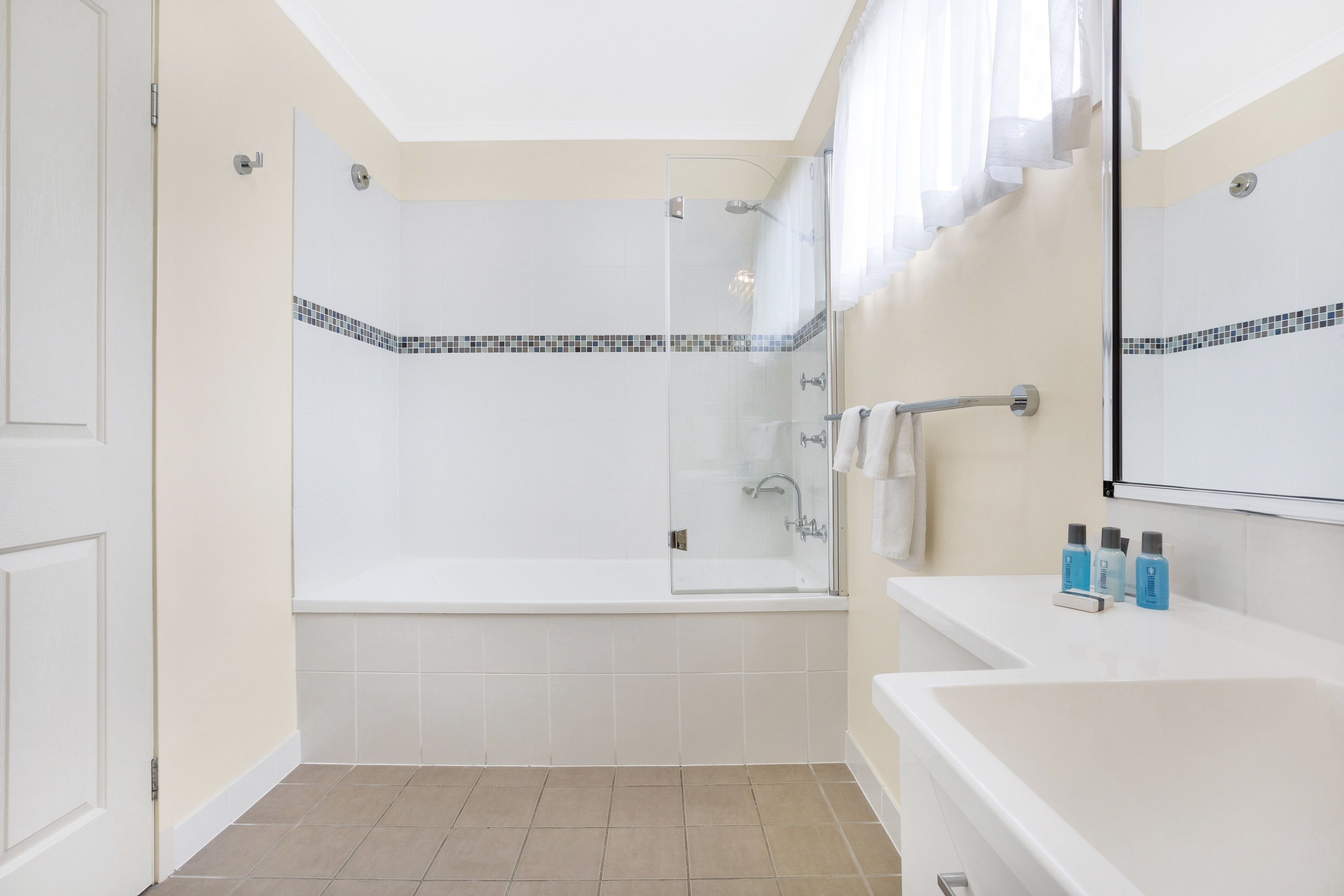 A modern bathroom with a glass-enclosed shower, a white bathtub, and a vanity with toiletries.