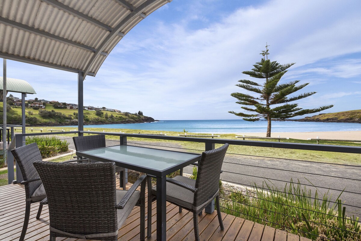 An outdoor patio with a table and chairs, overlooking a beach and ocean.