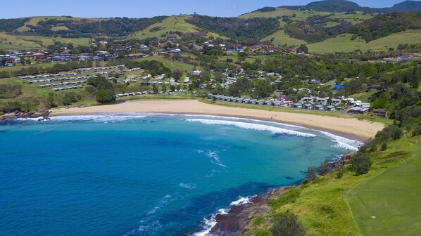 A coastal area with a beach, clear blue waters, and a residential area with houses and caravans. - Tasman Holiday Parks - Easts Beach (Kiama)