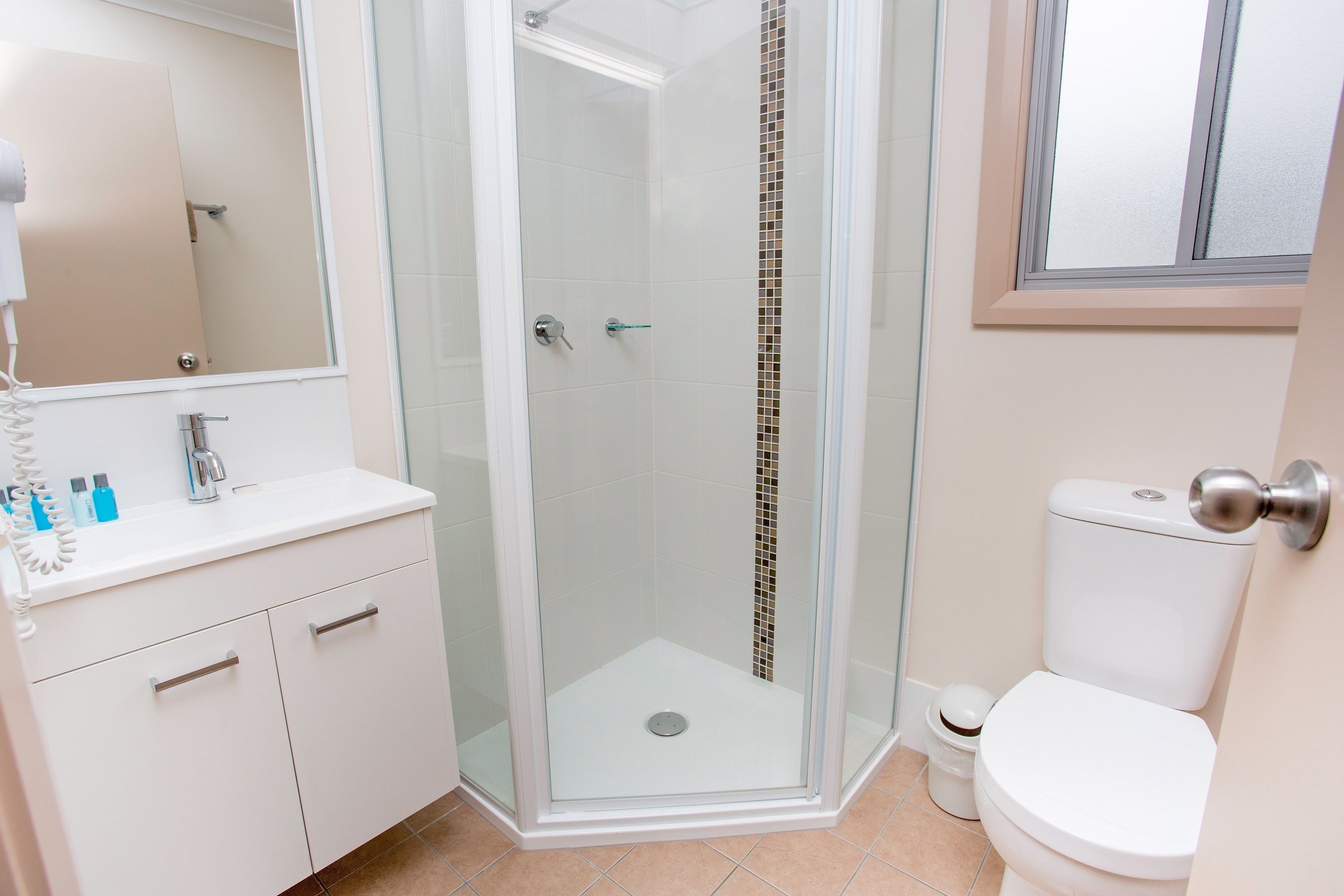 A modern bathroom with a glass-enclosed shower, a white sink with toiletries, and a toilet.