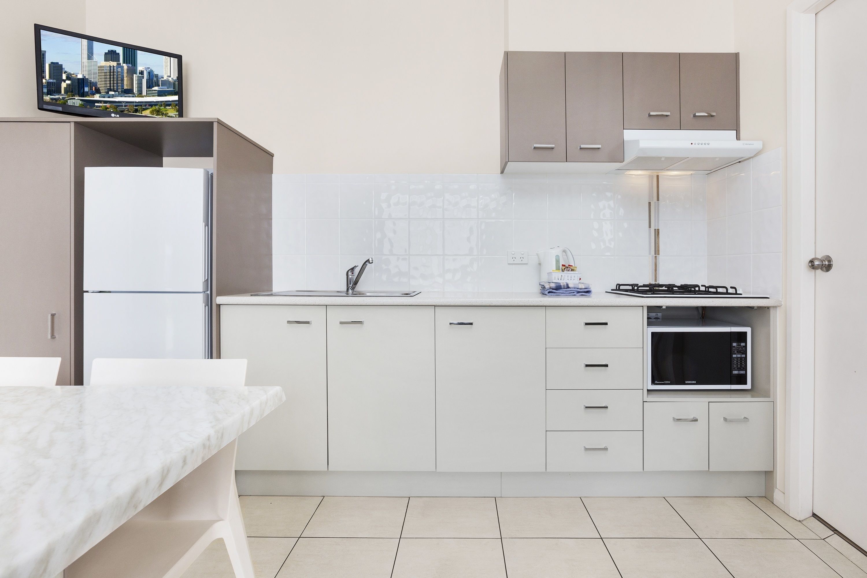 Una cocina moderna con armarios blancos, horno empotrado, microondas y televisor de pantalla plana sobre la encimera.